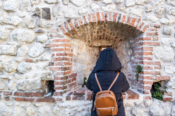 Κορίτσι από πίσω με κουκούλα γιλέκο, που αντιμετωπίζει ένα μεσαιωνικό αρχαίο τείχος - Φωτογραφία, εικόνα