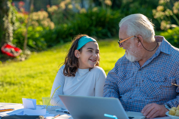 Nagyapa elmagyarázza, hogyan kell használni a laptopot az unokájának. - Fotó, kép