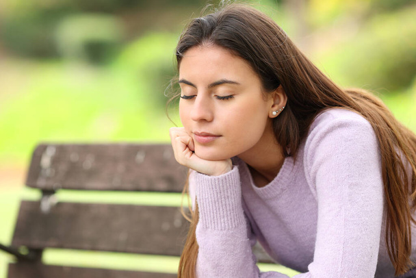 Relaxed teen resting with closed eyes sitting on a bench in a park - Foto, Imagem
