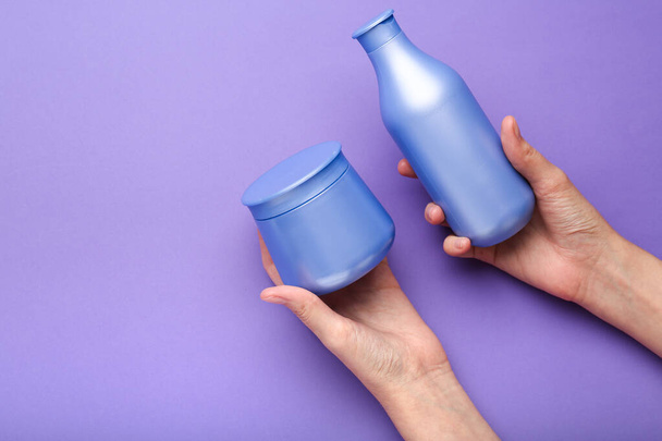 shampoo and hair mask in hands on a purple background. Minimalism, space for text. Top view - 写真・画像