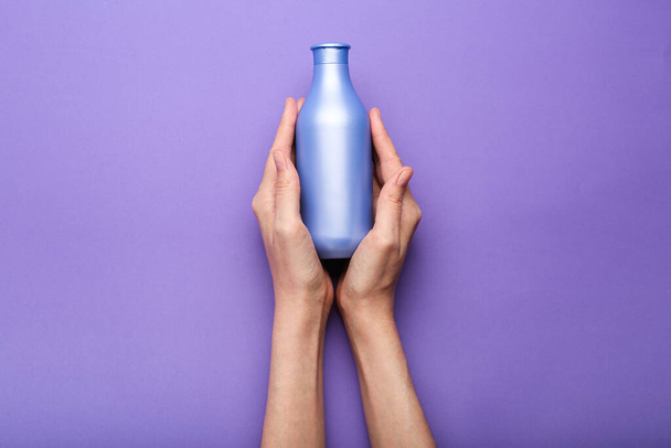 bottle of shampoo in hands on a purple background. Minimalism. Top view - Foto, afbeelding