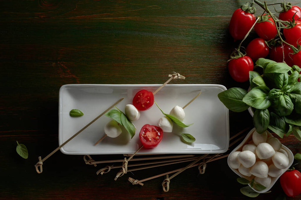 Mozzarella kaas met basilicum en tomaten op een donkergroene houten tafel. Bovenaanzicht. - Foto, afbeelding