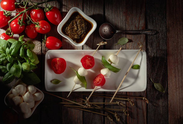Mozzarella met basilicum, pesto en tomaten op een oude houten tafel. Bovenaanzicht. - Foto, afbeelding