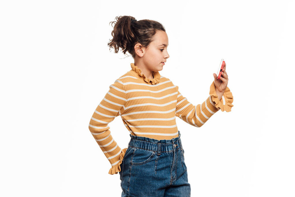 Menina usando um telefone celular enquanto está em pé sobre um fundo branco isolado. - Foto, Imagem
