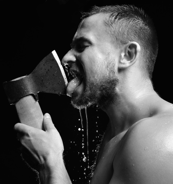 Bearded young man lick big axe foam and water splashes  - Фото, зображення