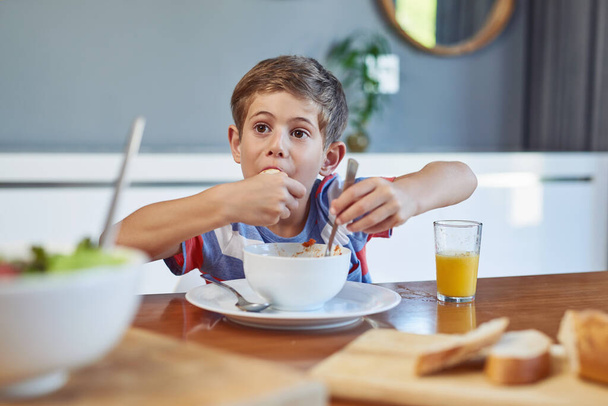 Це так смачно. Знімок чарівного маленького хлопчика, який насолоджується їжею вдома
. - Фото, зображення
