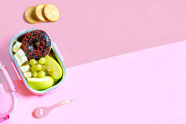 Catering food prepared in storage container with compartment with doughnut,apple,banana,cookies on pink background. meal with healthy balanced diet, lunch box boxed take away delivery packed ready. - Foto, Imagem