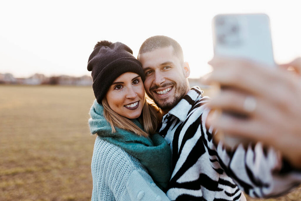 Couple taking a selfie photo with mobile phone in countryside at sunset - Photo, Image