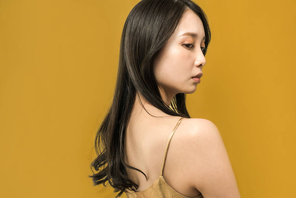 Black-haired woman standing in front of a golden background - 写真・画像