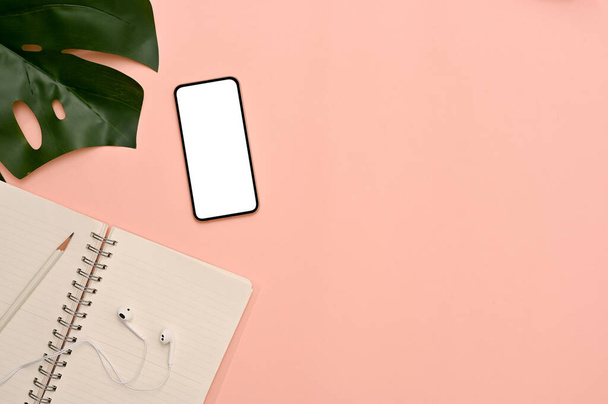 Flay lay, top view, Feminine workspace in pink background with stationery, earphones, monstera leaf, smartphone mockup and copy space. - Photo, Image