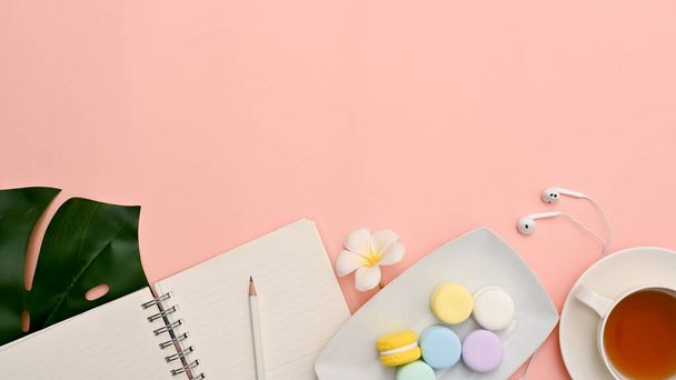 Pink pastel background with copy space for your presentation, stationery, a cup of tea, a plate of macaron and monstera leaf. top view - Foto, immagini