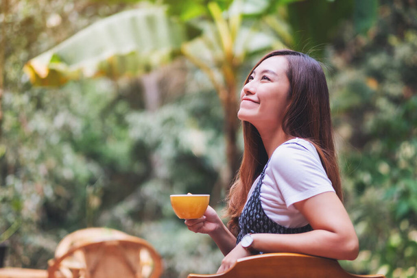 Closeup image of a beautiful asian woman holding and drinking hot coffee in the outdoors - Foto, imagen