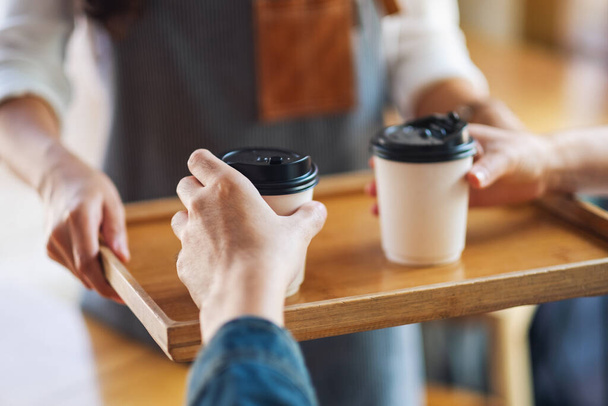 Servírka drží a slouží papírové šálky horké kávy pro zákazníka v kavárně - Fotografie, Obrázek