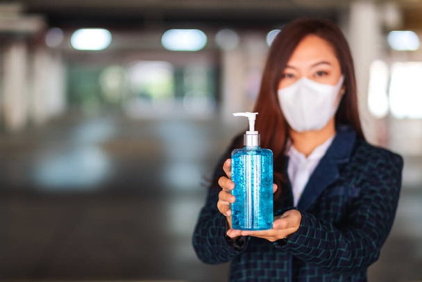 保護マスクを着用した女性のクローズアップ画像,保健医療用アルコールゲル消毒剤のボトルを保持し、示すCovid-19または2020ウイルスの概念 - 写真・画像