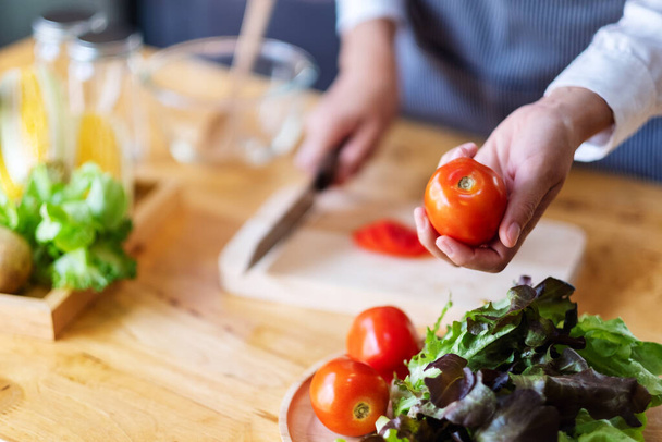Una chef sosteniendo y recogiendo un tomate fresco de una bandeja de verduras en la mesa - Foto, imagen