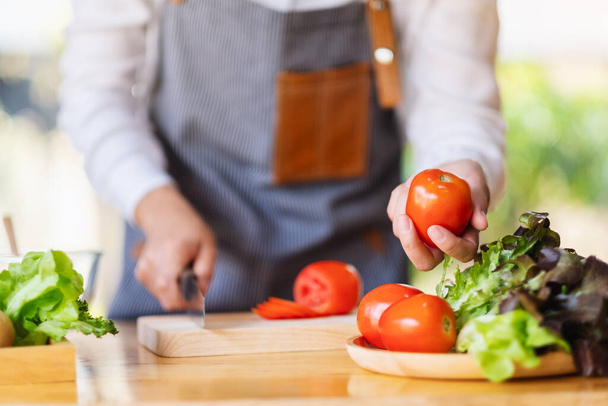 A woman chef holding and picking a fresh tomato from a vegetables tray on the table - Foto, imagen