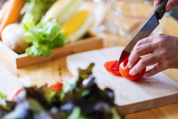 Wizerunek kobiety kucharza krojącego i krojącego pomidory nożem na drewnianej desce - Zdjęcie, obraz