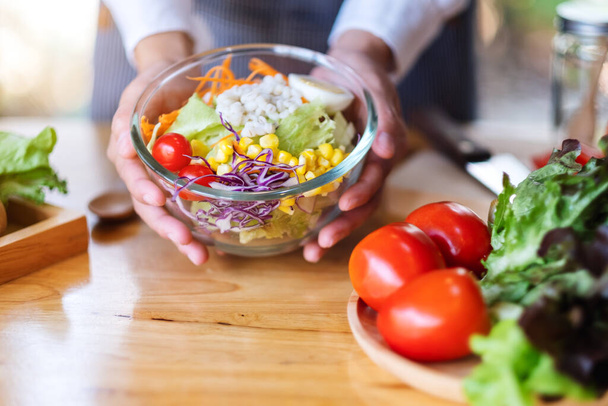 Lähikuva kuva naiskokki ruoanlaitto ja pitämällä kulhoon tuoreita sekoitettuja vihanneksia salaattia keittiössä - Valokuva, kuva