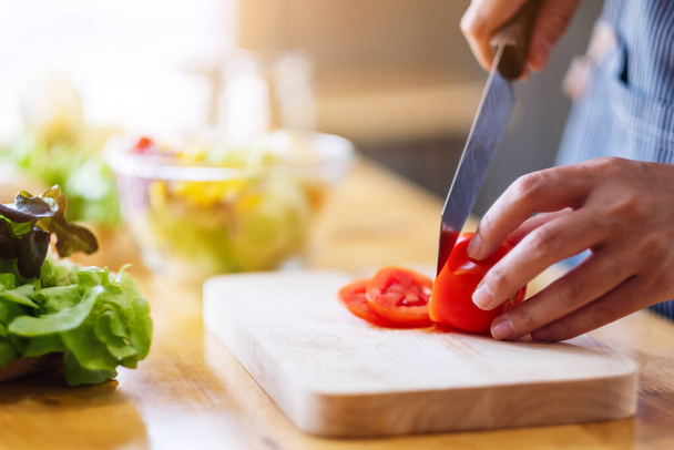 Nahaufnahme einer Köchin beim Schneiden und Schneiden von Tomaten mit dem Messer auf einem Holzbrett - Foto, Bild