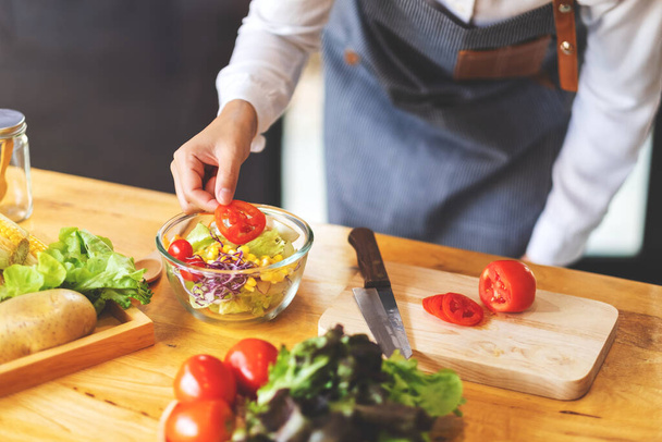 Immagine ravvicinata di una chef che cucina un'insalata di verdure miste fresche in cucina - Foto, immagini