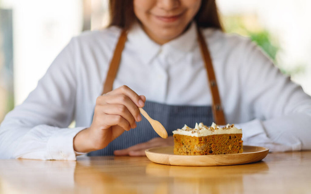 Una hermosa cocinera horneando y comiendo un pedazo de pastel de zanahoria casero en bandeja de madera - Foto, Imagen