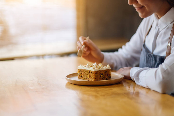 A beautiful female chef baking and eating a piece of homemade carrot cake in wooden tray - Fotoğraf, Görsel