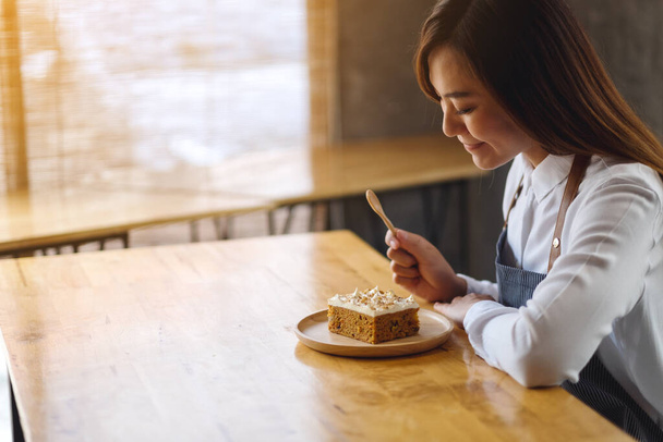 A beautiful female chef baking and eating a piece of homemade carrot cake in wooden tray - 写真・画像