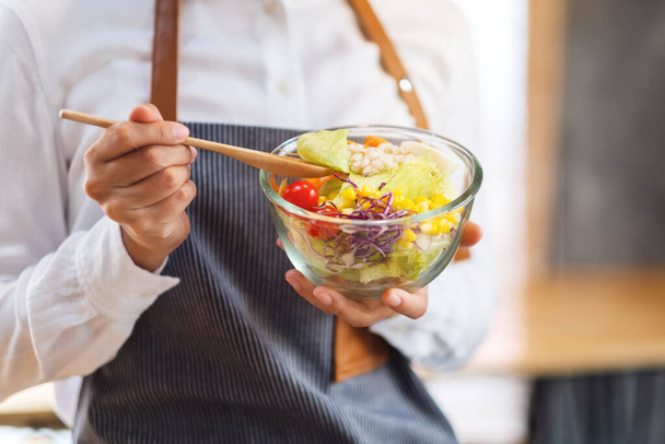 Close-up beeld van een vrouwelijke chef koken en het houden van een kom verse gemengde groenten salade om te eten in de keuken - Foto, afbeelding