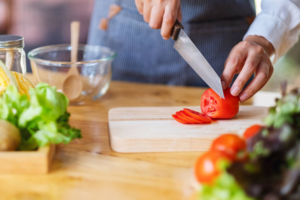 Imagen de cerca de una mujer chef cortando y picando tomate por cuchillo en una tabla de madera - Foto, Imagen