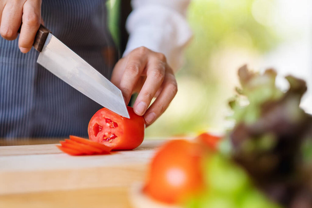 Immagine in primo piano di una donna chef che taglia e taglia il pomodoro con un coltello su tavola di legno - Foto, immagini