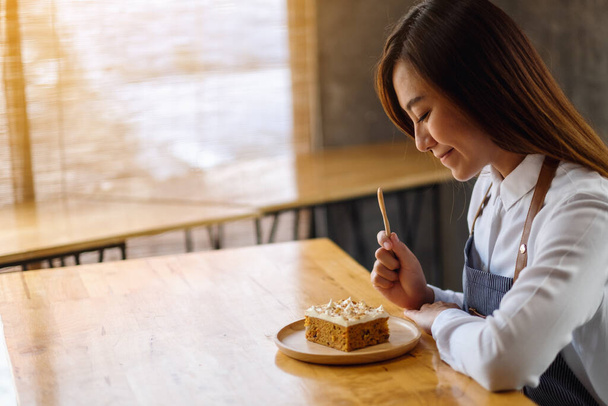 Красива жінка-кухарка випікає і їсть шматочок домашнього морквяного торта в дерев'яному лотку
 - Фото, зображення