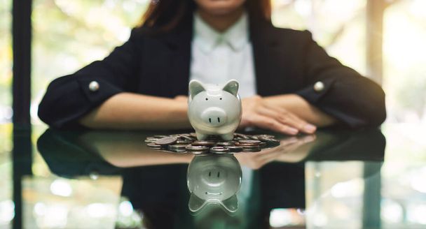 Closeup image of a business woman and a piggy bank on pile of coins for saving money concept - Photo, Image