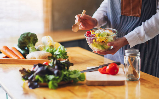 Szoros kép egy női séf főzés és gazdaság egy tál friss vegyes zöldség saláta enni a konyhában - Fotó, kép