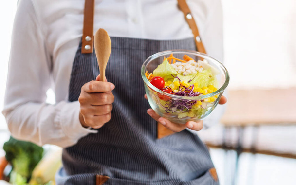 Lähikuva kuva naispuolinen kokki ruoanlaitto ja pitämällä kulhoon tuoreita sekoitettuja vihanneksia salaattia syödä keittiössä - Valokuva, kuva