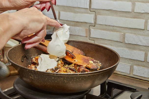 Šéf nalévá čerstvou smetanu do pánve se smaženými brambory, kaštany, petrželkou, parmezánem a dřevěnými stěrkami na plynových kamnech. Krok za krokem recept - Fotografie, Obrázek
