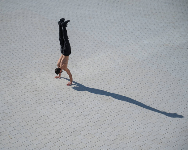 Shirtless man walks on his hands outdoors. View from above. - Foto, imagen
