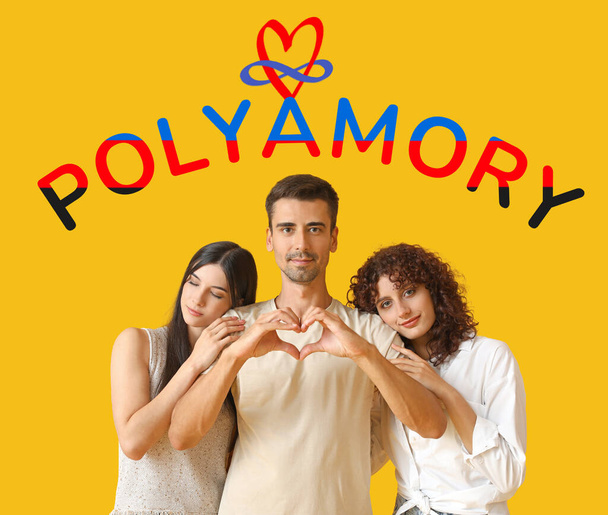 Man with two beautiful women and word POLYAMORY on orange background - Foto, Imagen