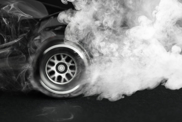 Modern racing car with smoke from under wheels on dark background, closeup - Foto, Imagen