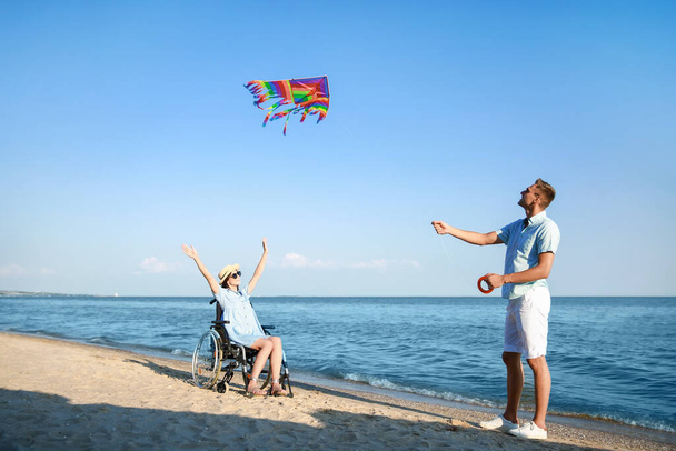 Young woman with physical disability and her boyfriend flying kite at sea resort - Photo, Image