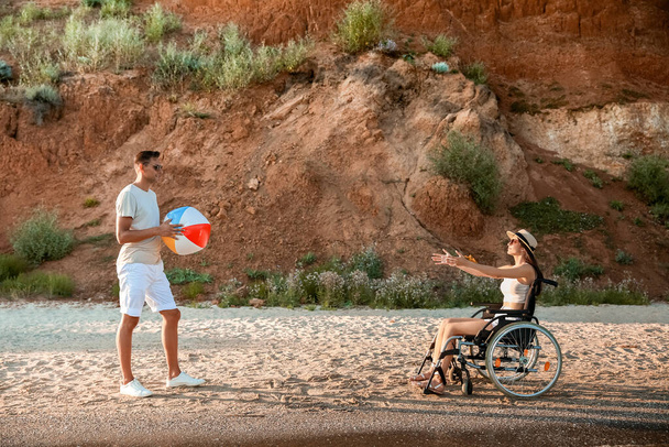Ευτυχισμένη γυναίκα με σωματική αναπηρία και ο φίλος της παίζει με μπάλα στο θέρετρο της θάλασσας - Φωτογραφία, εικόνα