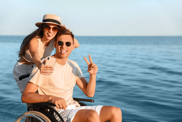 Ευτυχισμένος άντρας με σωματική αναπηρία και η κοπέλα του να βγάζει σέλφι στο θέρετρο. - Φωτογραφία, εικόνα
