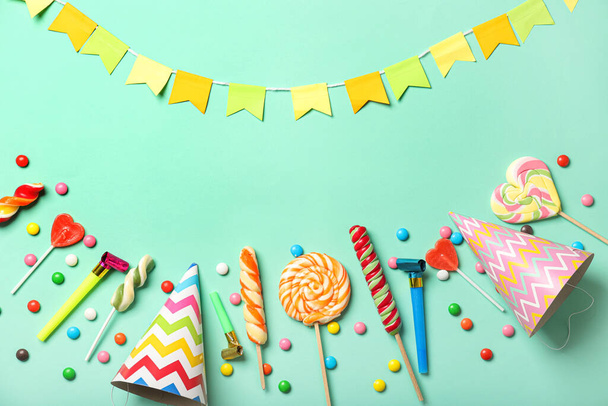 Komposition mit süßen Lutschern und Geburtstagsmützen auf farbigem Hintergrund - Foto, Bild