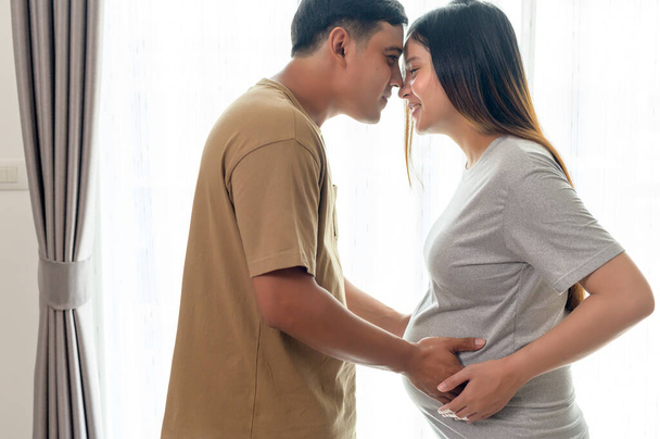 Genç hamile bir kadın kocasıyla kucaklaşıyor ve evde bir bebek bekliyor. - Fotoğraf, Görsel