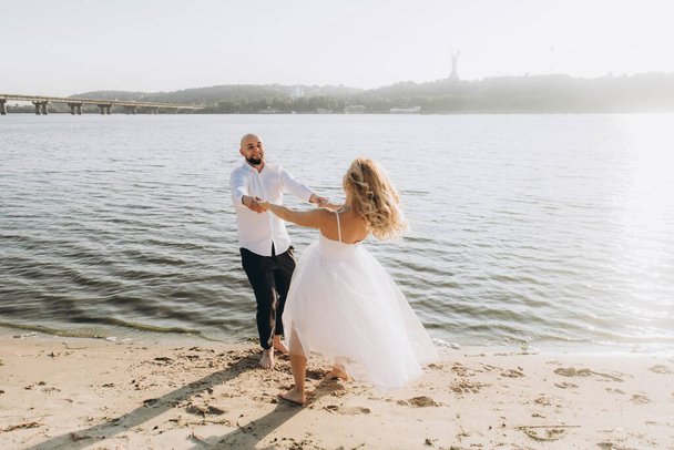 Wedding photosession at sunset of a beautiful couple, the bride in a white dress, and the groom in a white shirt and black trousers - Фото, изображение