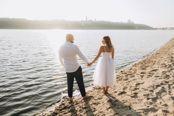 Wedding photosession at sunset of a beautiful couple, the bride in a white dress, and the groom in a white shirt and black trousers - Zdjęcie, obraz