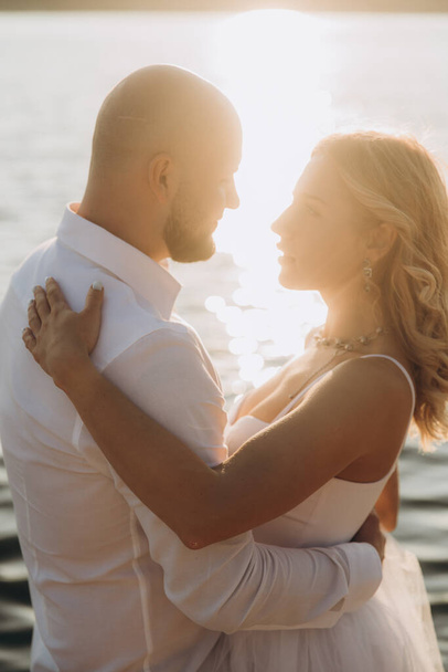 Wedding photosession at sunset of a beautiful couple, the bride in a white dress, and the groom in a white shirt and black trousers - Фото, зображення