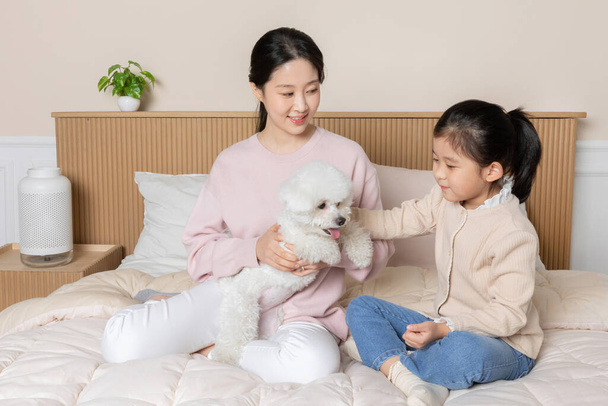 Asian Korean mother and daughter and puppy dog sitting on bed - Foto, imagen