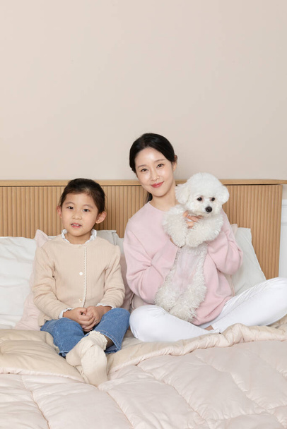 Asian Korean mother and daughter and puppy dog sitting on bed - Zdjęcie, obraz