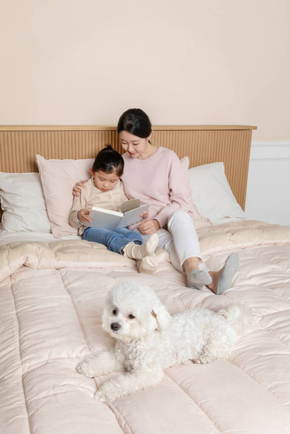 Asian Korean mother and daughter and puppy dog reading in bed - Valokuva, kuva