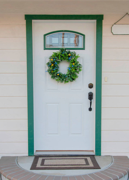 Függőleges fehér bejárati ajtó egy hajlított ajtókkal rendelkező házban Oceanside-ban, Kaliforniában. Első külső fehér vinil körrel és fehér ajtóval, zöld ajtókerettel és koszorúval. - Fotó, kép